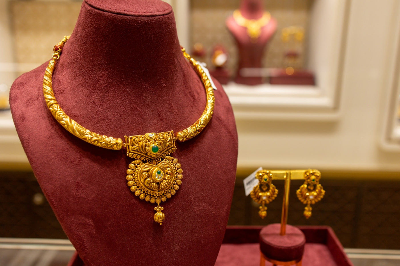 A gold kanthi necklace on maroon velvet in a Vasundhra Raj Luxury Jewellery store