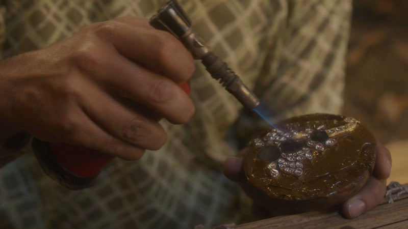 A karigar warms a piece set on lac with a small flame