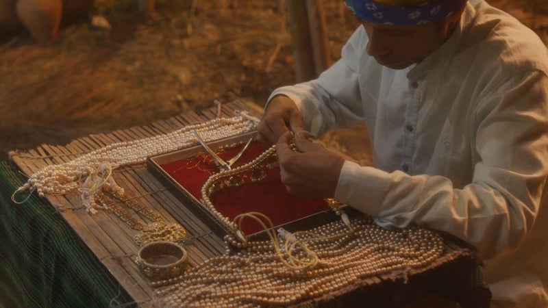 A karigar strings pearls into a necklace