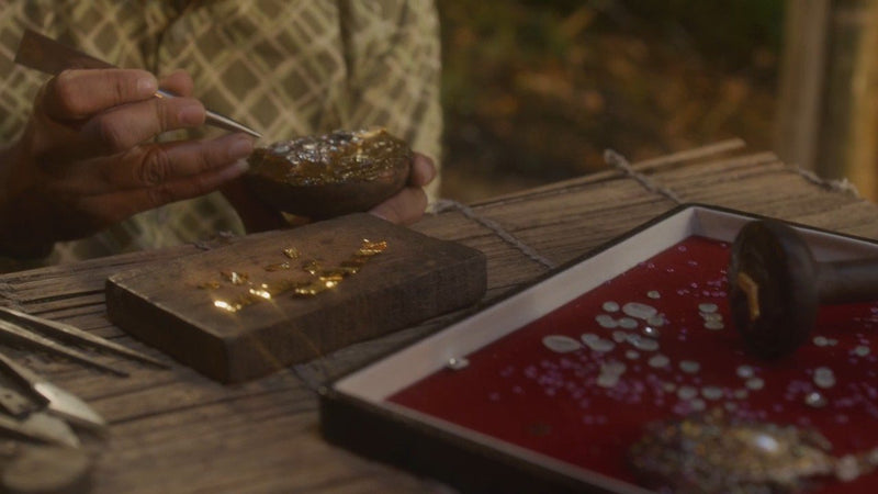 A karigar sets a stone with fine tweezers beside a tray of polki